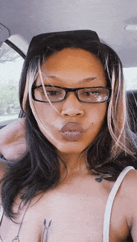 a woman wearing glasses is sitting in a car and making a funny face .