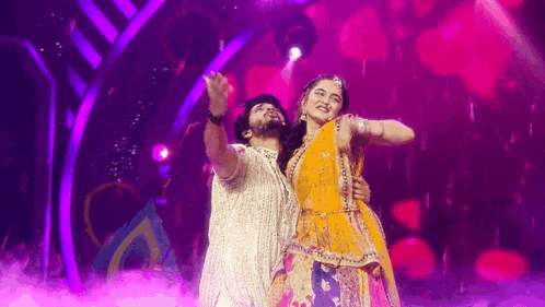 a man and a woman are dancing on a stage with purple lights behind them .
