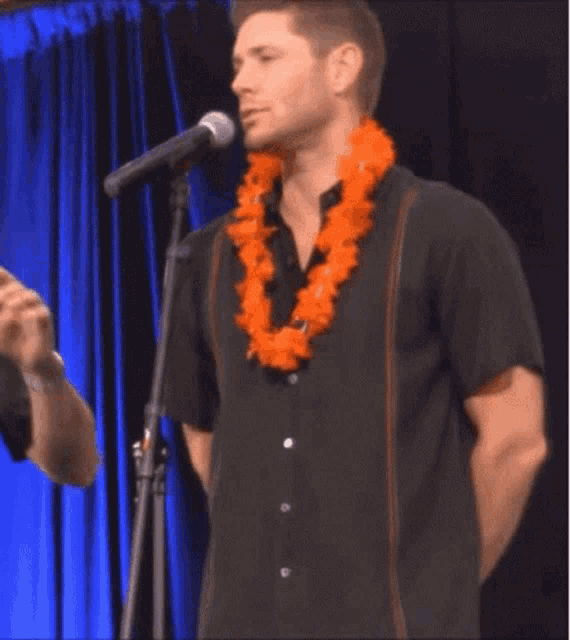 a man wearing a hawaiian lei is standing in front of a microphone .