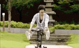 a man is riding a bike in a park with a statue in the background