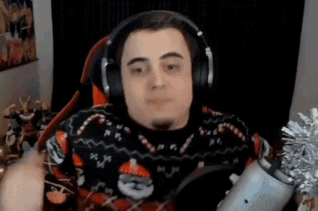 a man wearing headphones and a christmas sweater is sitting in a chair in front of a microphone .