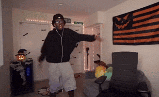 a man wearing headphones is dancing in a room with an orange and black flag hanging on the wall