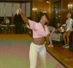 a woman in a pink shirt and white pants is dancing in a room .