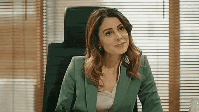 a woman in a green suit is sitting at a desk in an office .