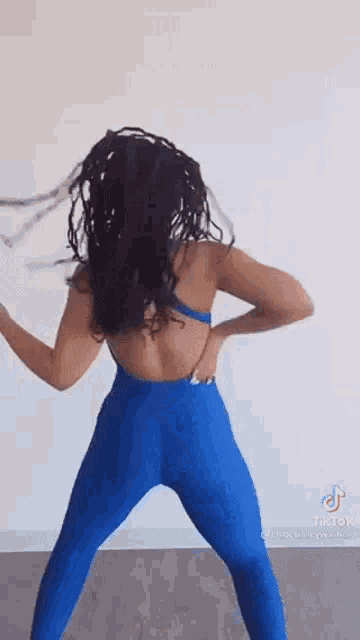 a woman in a blue jumpsuit is dancing in a room with her hair blowing in the wind .