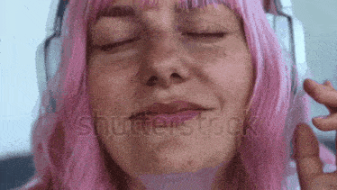 a woman with pink hair and freckles is making a funny face while wearing headphones .