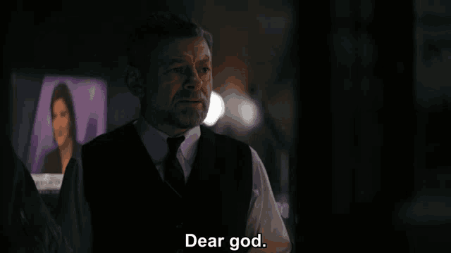 a man in a suit and tie says dear god in a dark room