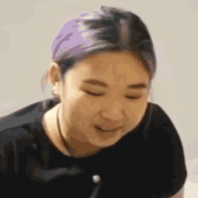 a woman with purple hair is wearing a black shirt and a necklace .