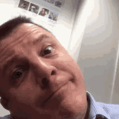 a man is making a funny face in front of a wall with a picture of a woman on it .