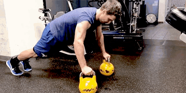 a man in a blue shirt is doing push ups with a yellow kettlebell