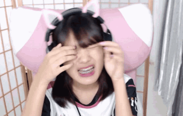 a young girl wearing headphones and cat ears wipes her eyes