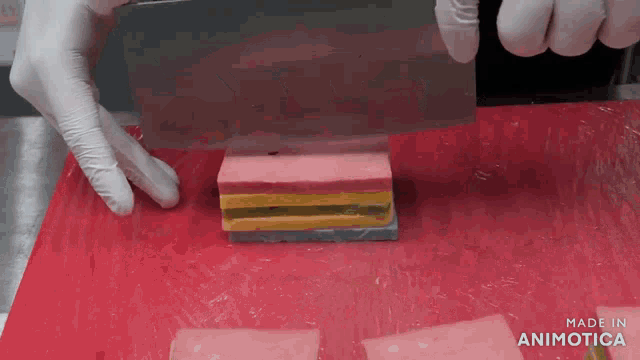 a person is cutting a piece of candy with a knife on a red cutting board made in animatica