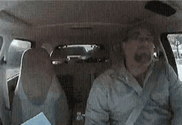 a man is sitting in the back seat of a car holding a book .