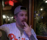 a man wearing a phillies jersey holds his finger to his lips