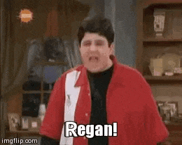 a man in a red shirt is standing in a living room with his mouth open .