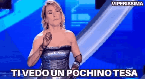 a woman in a strapless dress is singing into a microphone with the words ti vedo un pochino tesa written below her