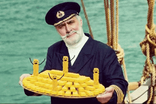 a man in a captain 's uniform is holding a tray of food with smiley faces on it .