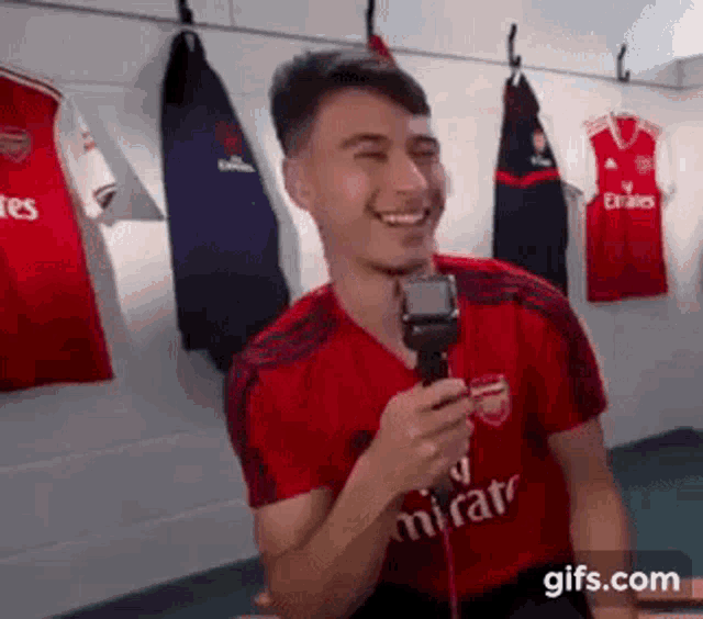 a man in a red emirates shirt is holding a microphone and smiling .