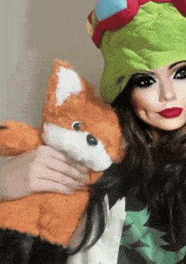 a woman in a green hat holds a stuffed fox