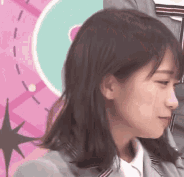 a close up of a woman 's face with a pink background and a clock in the background .