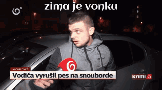 a man with a microphone in front of a car with the words zima je vonku below him