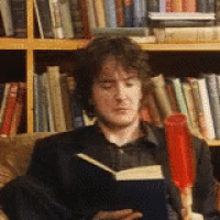 a man in a suit is reading a book in front of a bookshelf