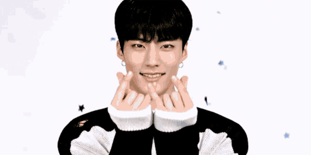 a young man wearing a black and white sweater is making a heart with his hands