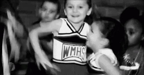 a black and white photo of a little girl in a cheerleading uniform being held by a girl .
