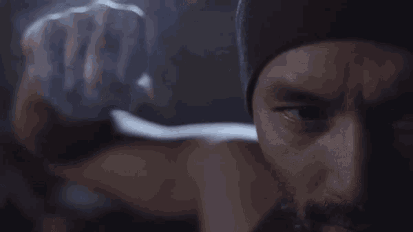 a close up of a man 's face with a beard wearing a hat and a fist in the air .
