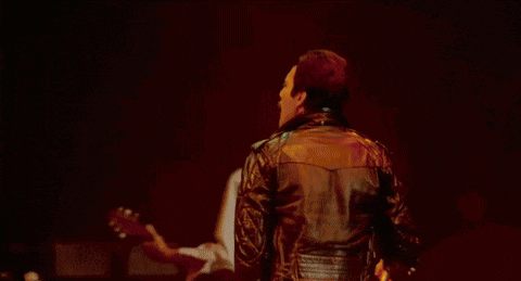 a man singing into a microphone on a stage with a drum set behind him