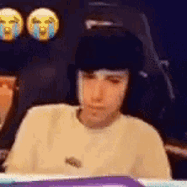a man wearing headphones is sitting in front of a computer screen with a sad face on it .