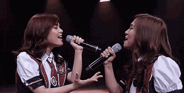 two girls are singing into microphones and one has the number 49 on her shirt