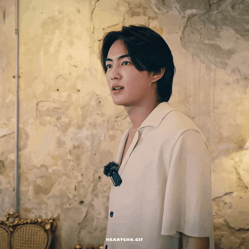 a man in a white shirt is standing in front of a wall with the words heartchu.gif written on the bottom