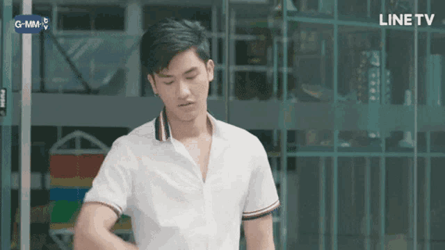 a young man in a white shirt is standing in front of a building with a line tv logo in the background .