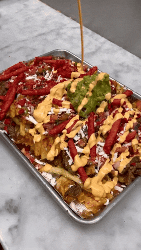 a tray of nachos with guacamole being poured on top