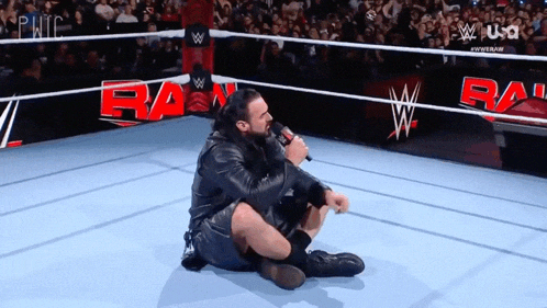a man is kneeling down in a wrestling ring with a microphone .