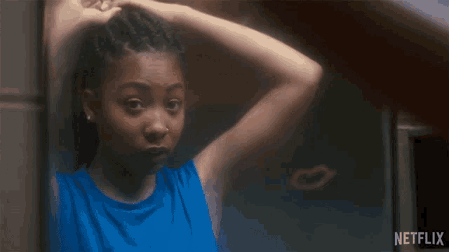 a woman in a blue tank top is looking at herself in a mirror with netflix written on the bottom right