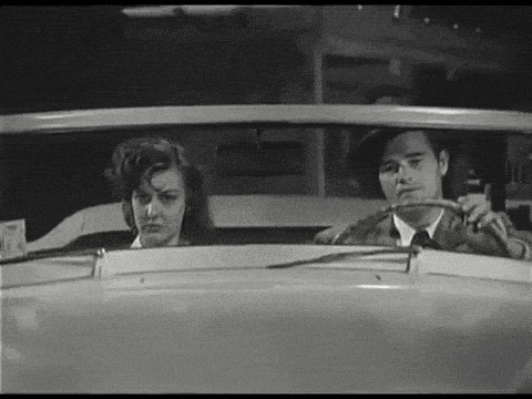 a man and a woman are sitting in a car looking out the window