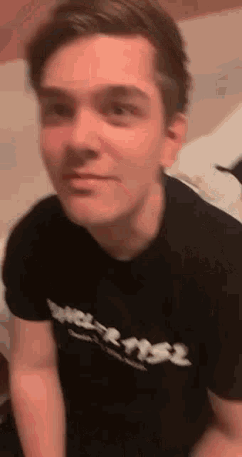a young man wearing a black t-shirt is sitting on a bed and making a funny face .