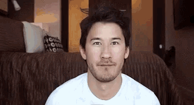 a man with a beard and a white shirt is sitting on a couch .