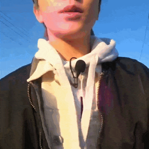 a person wearing a black jacket and a white hoodie with a microphone around their neck