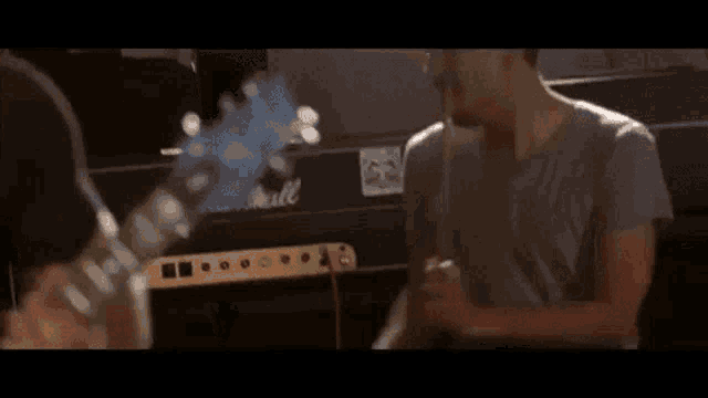 a man playing a guitar and a man playing drums are shaking hands in front of a marshall amplifier .