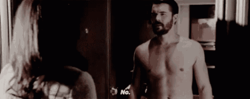 a man without a shirt is standing next to a woman in front of a mirror .