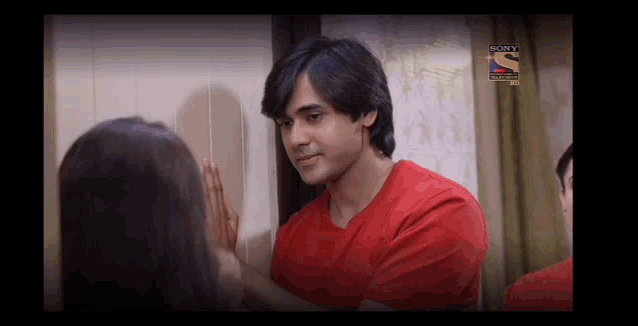 a man in a red shirt is touching a woman 's face in front of a sony logo