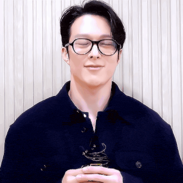 a man wearing glasses and a blue shirt is smiling with his eyes closed .