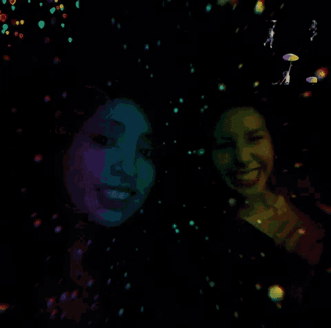 two women are standing next to each other in a dark room with glowing lights behind them