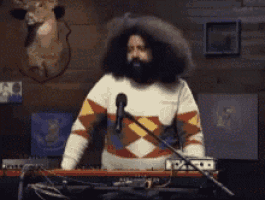 a man with a beard is playing a keyboard and talking into a microphone