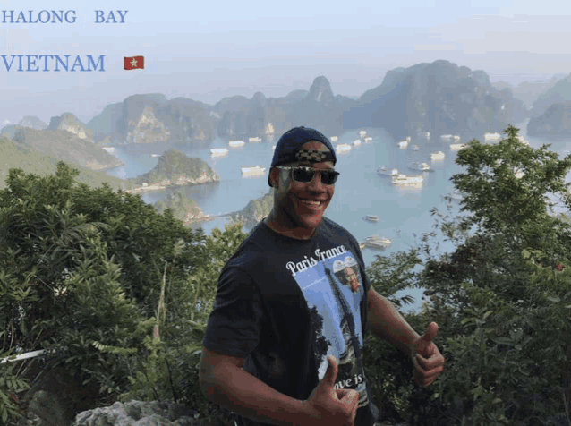a man wearing sunglasses and a paris france shirt stands in front of a bay in vietnam