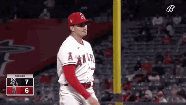 a baseball player is standing on the field during a game with a scoreboard behind him .