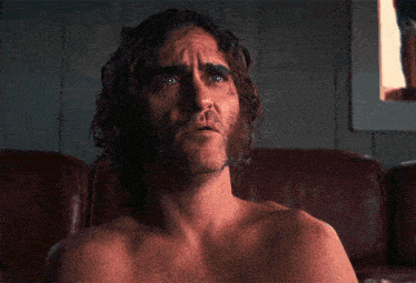 a shirtless man covering his face with his hands in a dark room